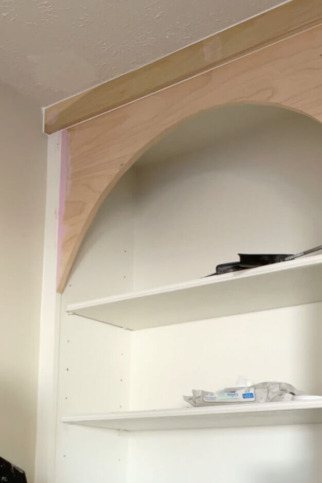 Using caulk and wood filler to finish a DIY arched shelf.